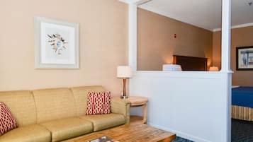 A hotel room with a beige sofa, a wooden coffee table, a small side table with a lamp, and a framed picture on the wall.