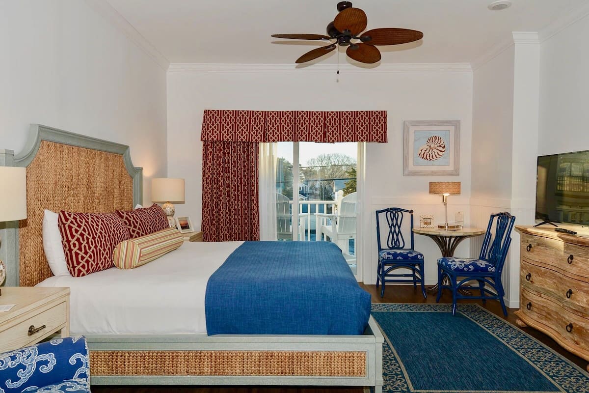 A hotel room with a bed, two chairs, a small table, a dresser, and a ceiling fan.