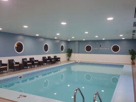 A swimming pool with a blue tiled floor, surrounded by lounge chairs and a wall with circular windows.