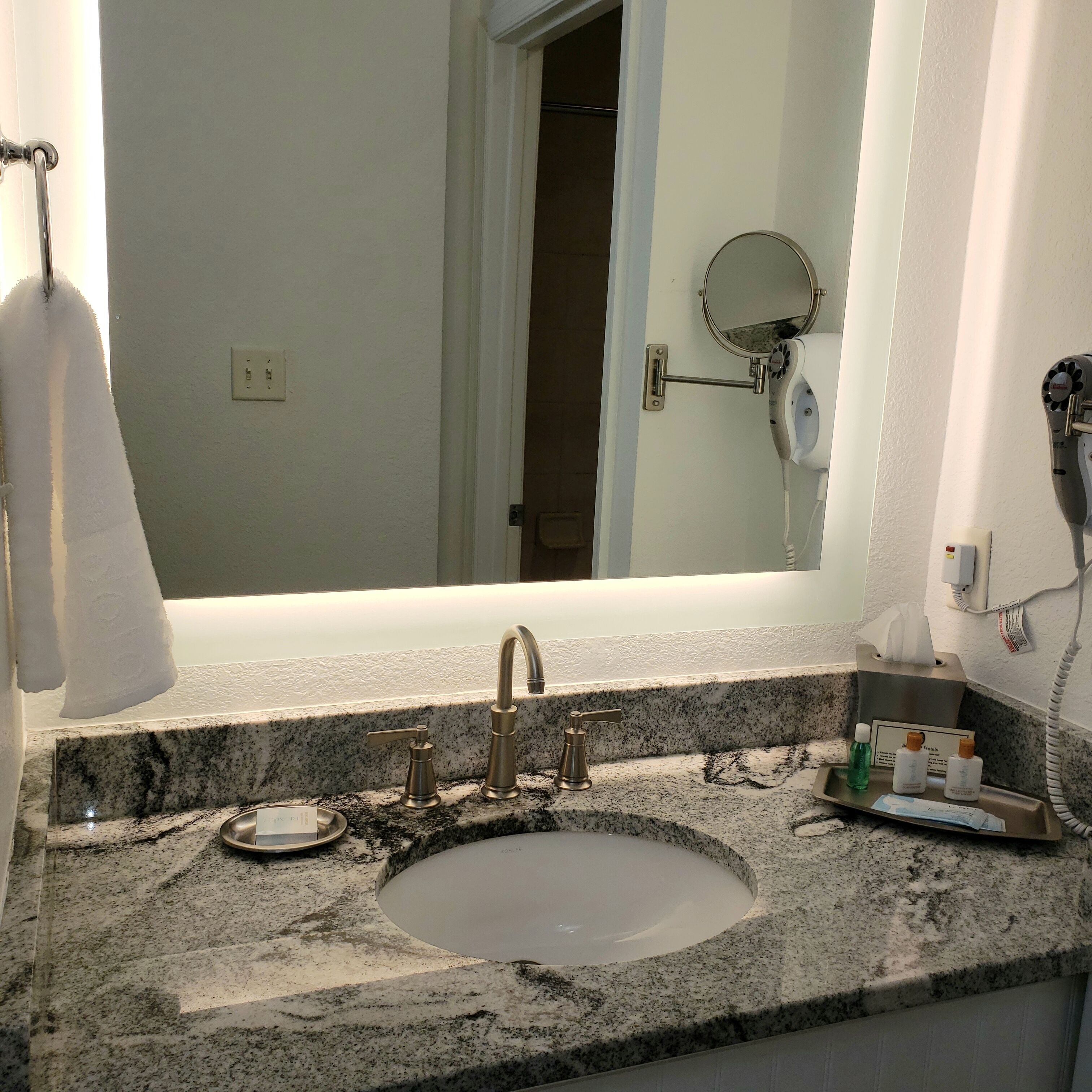A bathroom with a granite countertop, a sink, a mirror, and a hairdryer mounted on the wall.