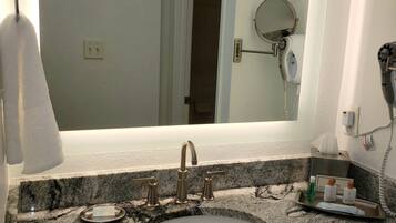 A bathroom with a granite countertop, a sink, a mirror, and a hairdryer mounted on the wall.