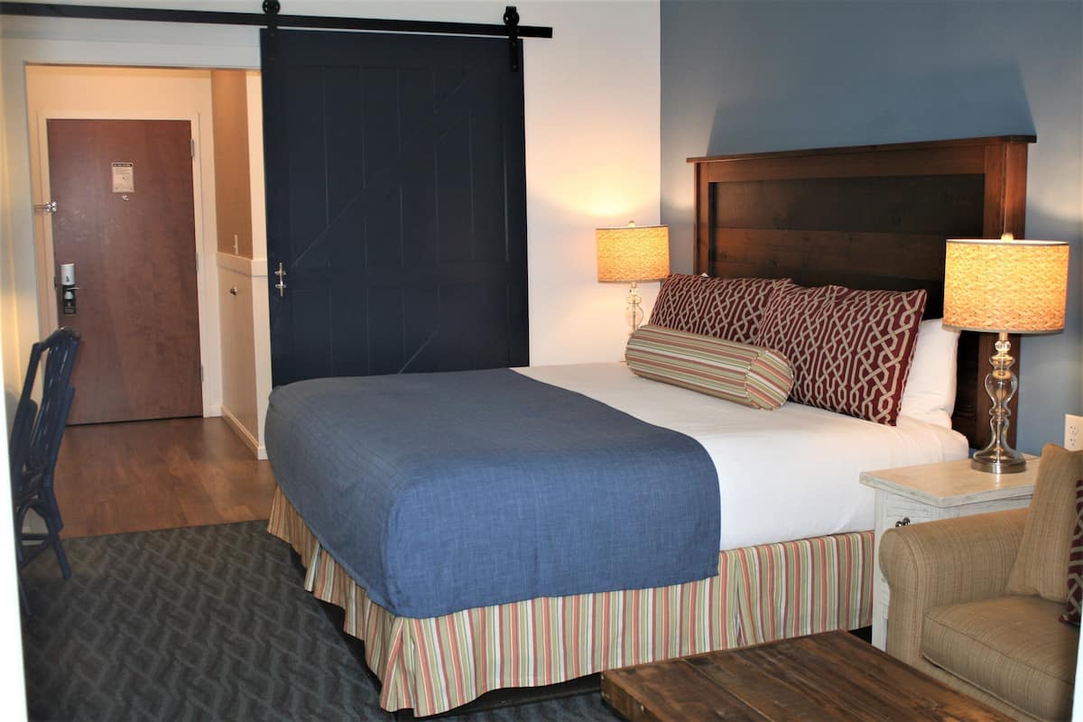 A hotel room with a large bed, two bedside lamps, a wooden headboard, a striped bench, and a door with a lock.