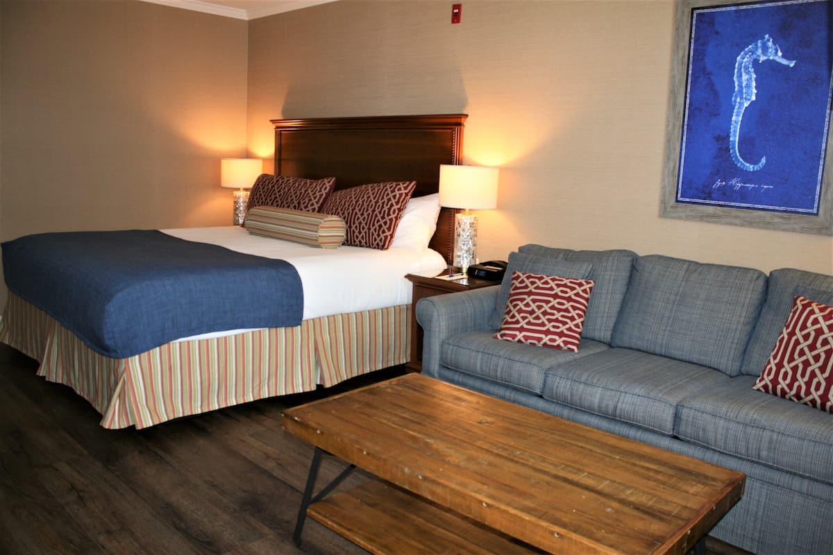 A hotel room with a double bed, a sofa, a wooden coffee table, and a framed seahorse artwork on the wall.