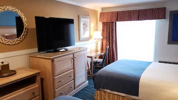 Quarto de hotel com televisão de tela plana, escrivaninha com abajur, uma cadeira e uma cama.