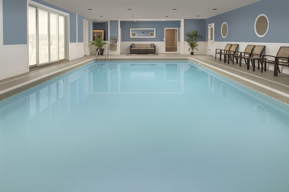 A large indoor swimming pool with a bench and chairs along the side, a reception area with a couch, and large windows.