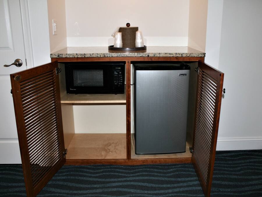 A compact kitchen with a microwave and refrigerator, wooden cabinets, and a countertop.