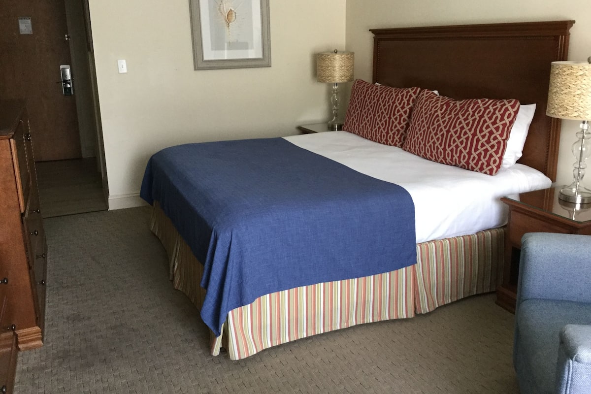 A hotel room with a bed, a nightstand, a lamp, and a framed picture on the wall.
