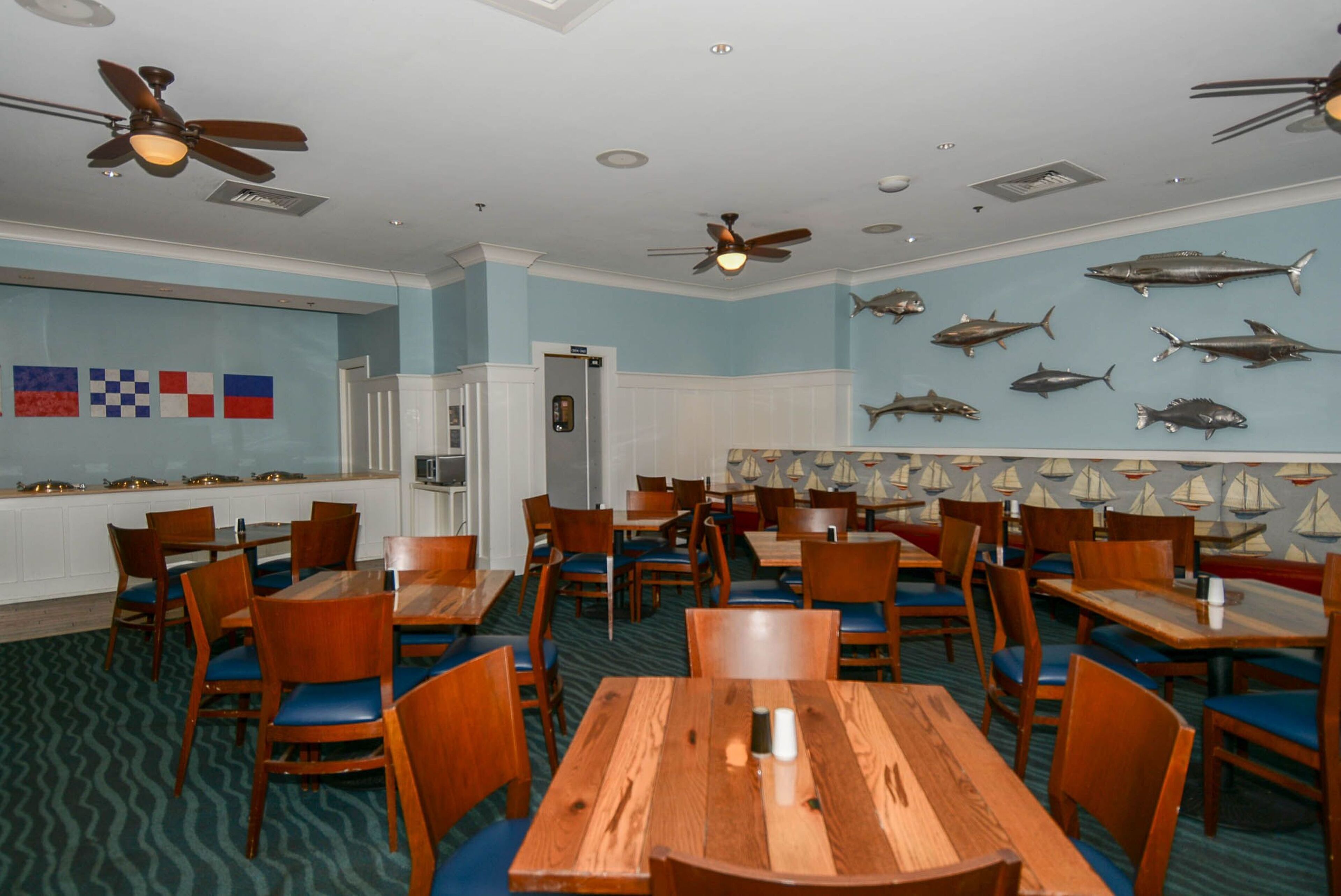 A restaurant with wooden tables and chairs, ceiling fans, and fish wall decorations.