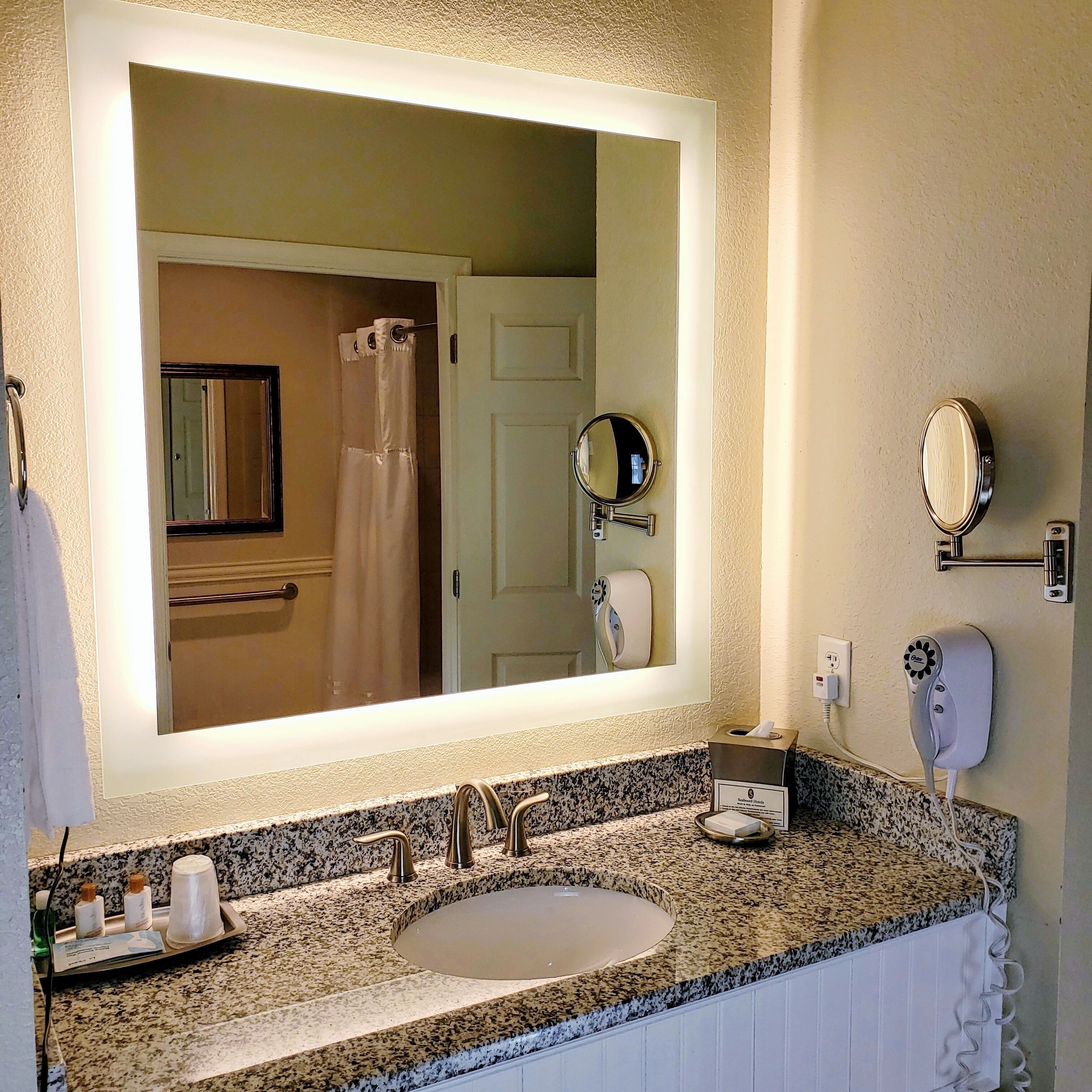A bathroom with a large mirror, a sink, a towel rack, a hairdryer, and a toilet paper holder.
