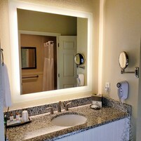 Ein Badezimmer mit großem Spiegel, Waschbecken, Handtuchhalter, Haartrockner und Toilettenpapierhalter.