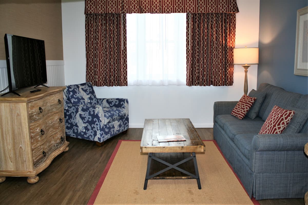 A living room with a sofa, armchair, wooden coffee table, and a TV on a wooden cabinet.