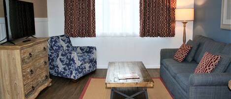 Una sala de estar con sofá, sillón, mesa de centro de madera y televisor sobre un mueble de madera.