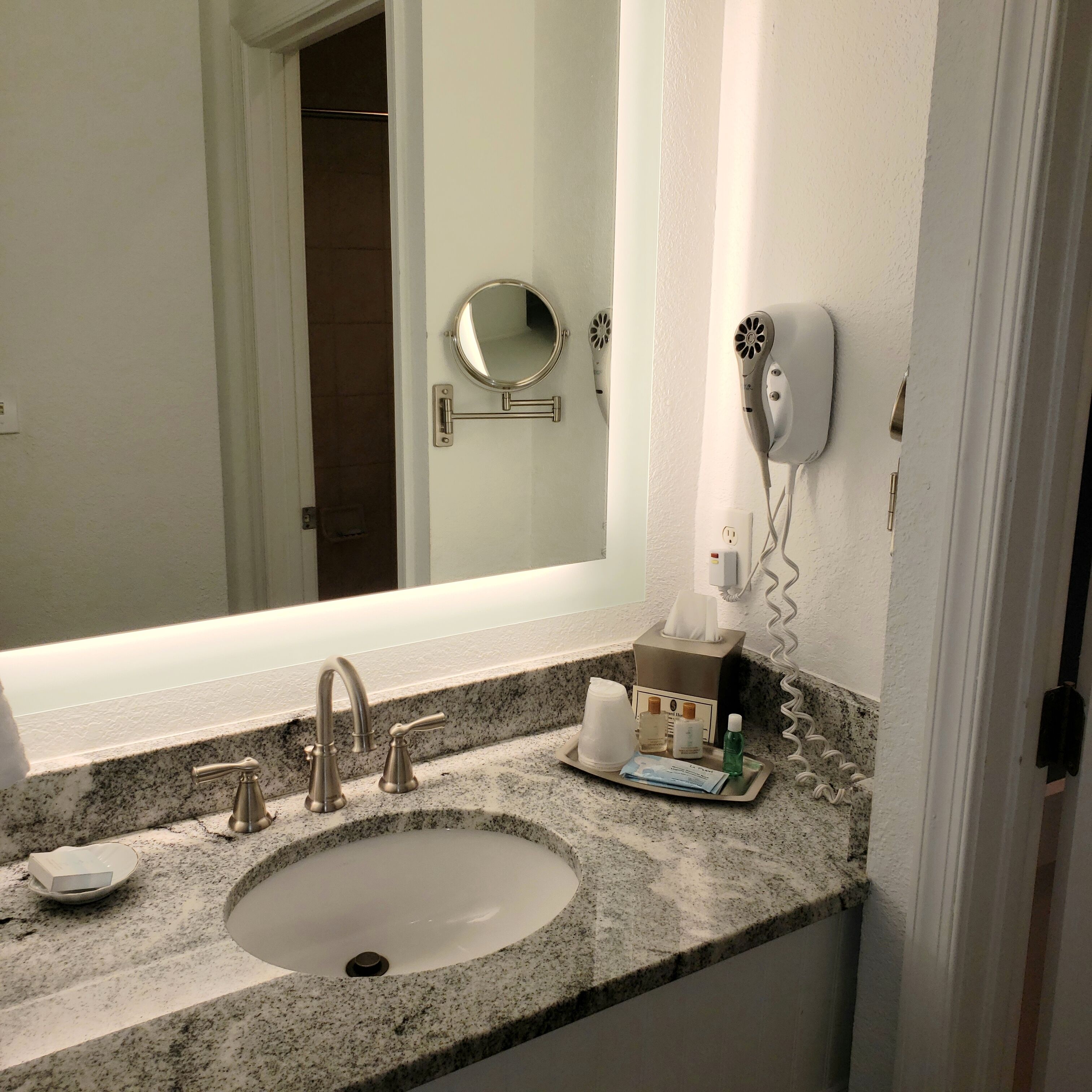 A bathroom with a sink, mirror, hairdryer, and toiletries.