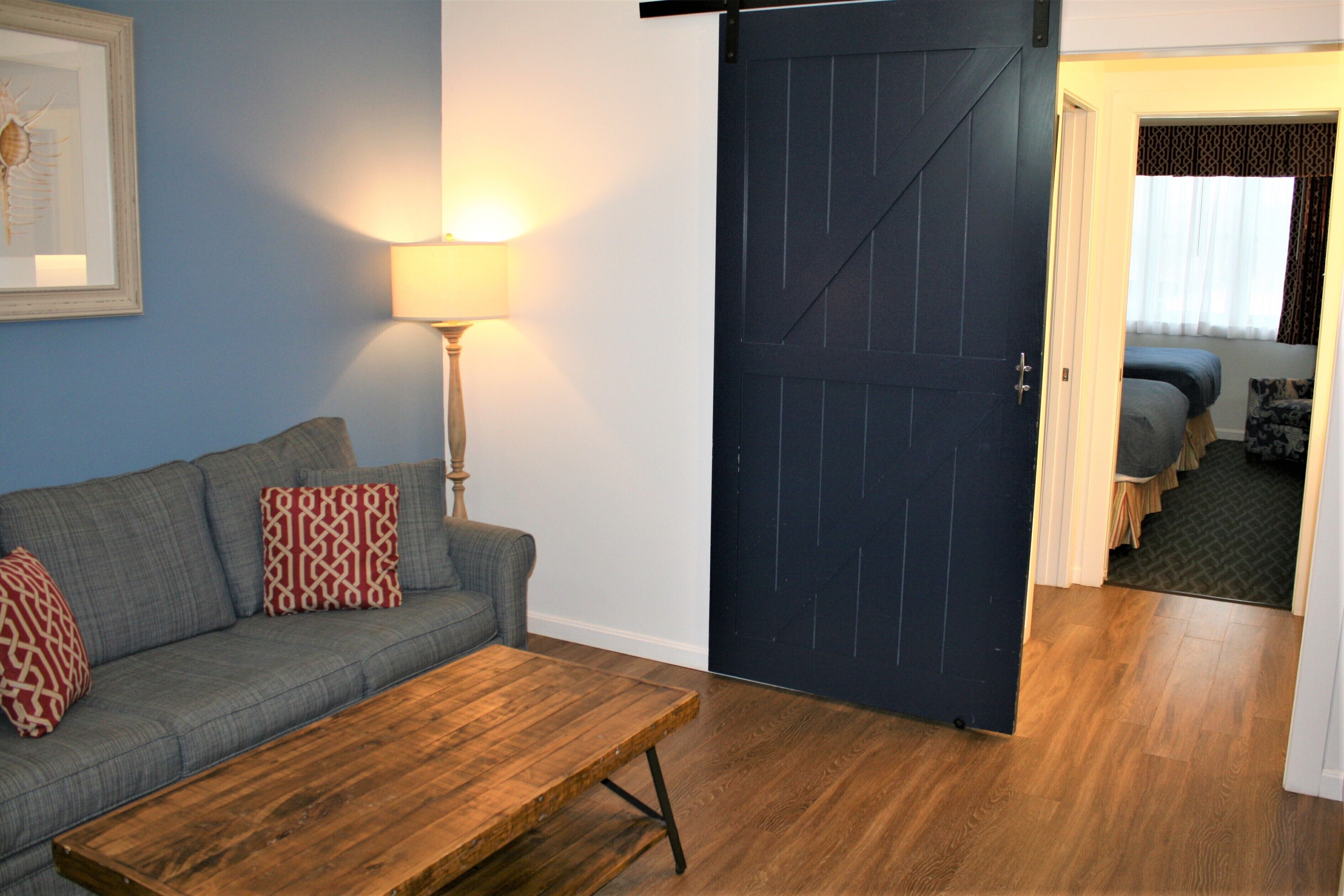 A room with a sofa, a wooden coffee table, a lamp, and a dark door leading to another room.