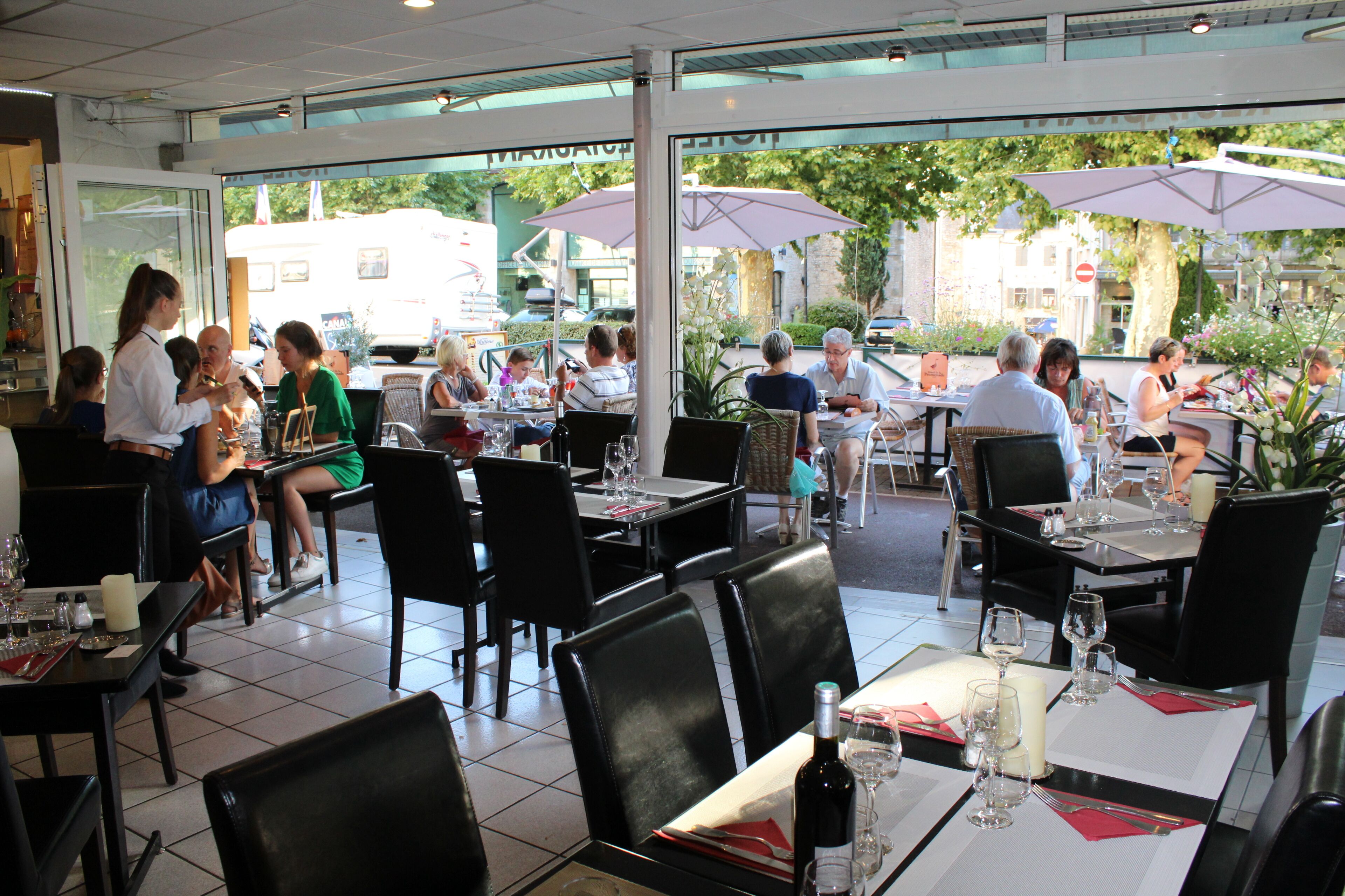An outdoor dining area with tables and chairs, umbrellas, and a view of the street.