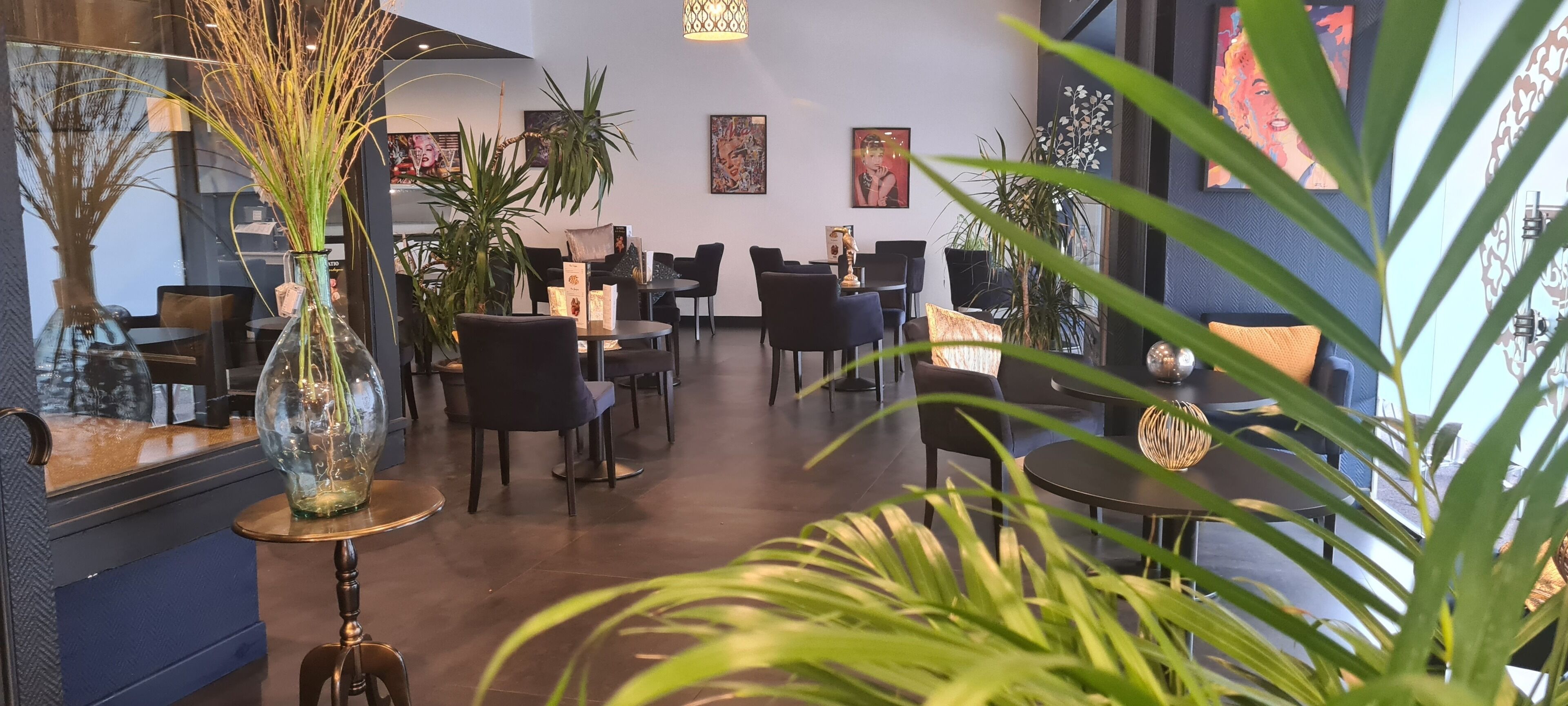 Un intérieur de restaurant moderne avec des tables rondes, des chaises noires et des plantes en pot.