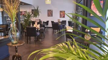 Un intérieur de restaurant moderne avec des tables rondes, des chaises noires et des plantes en pot.
