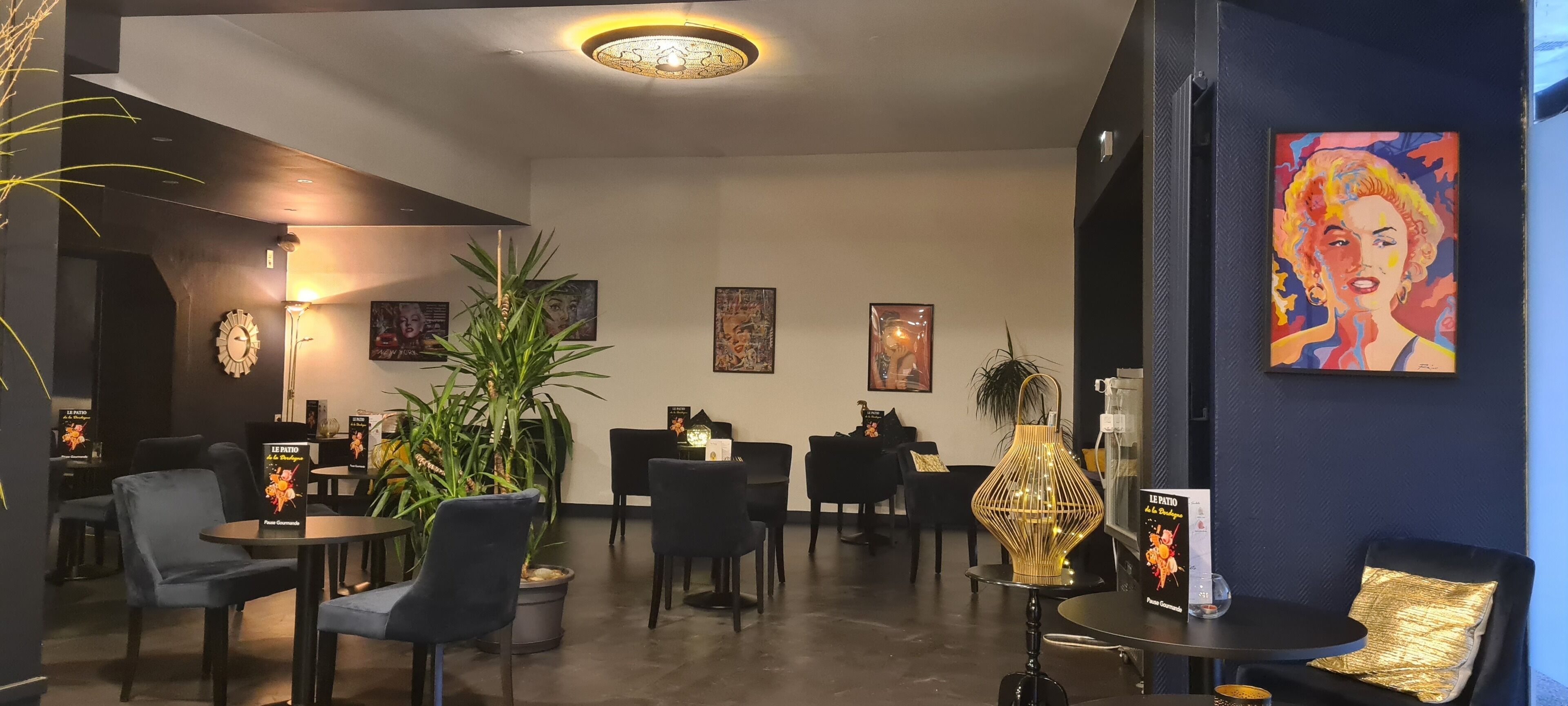 A modern lounge area with black furniture, a large potted plant, and artwork on the walls.