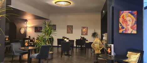A modern lounge area with black furniture, a large potted plant, and artwork on the walls.