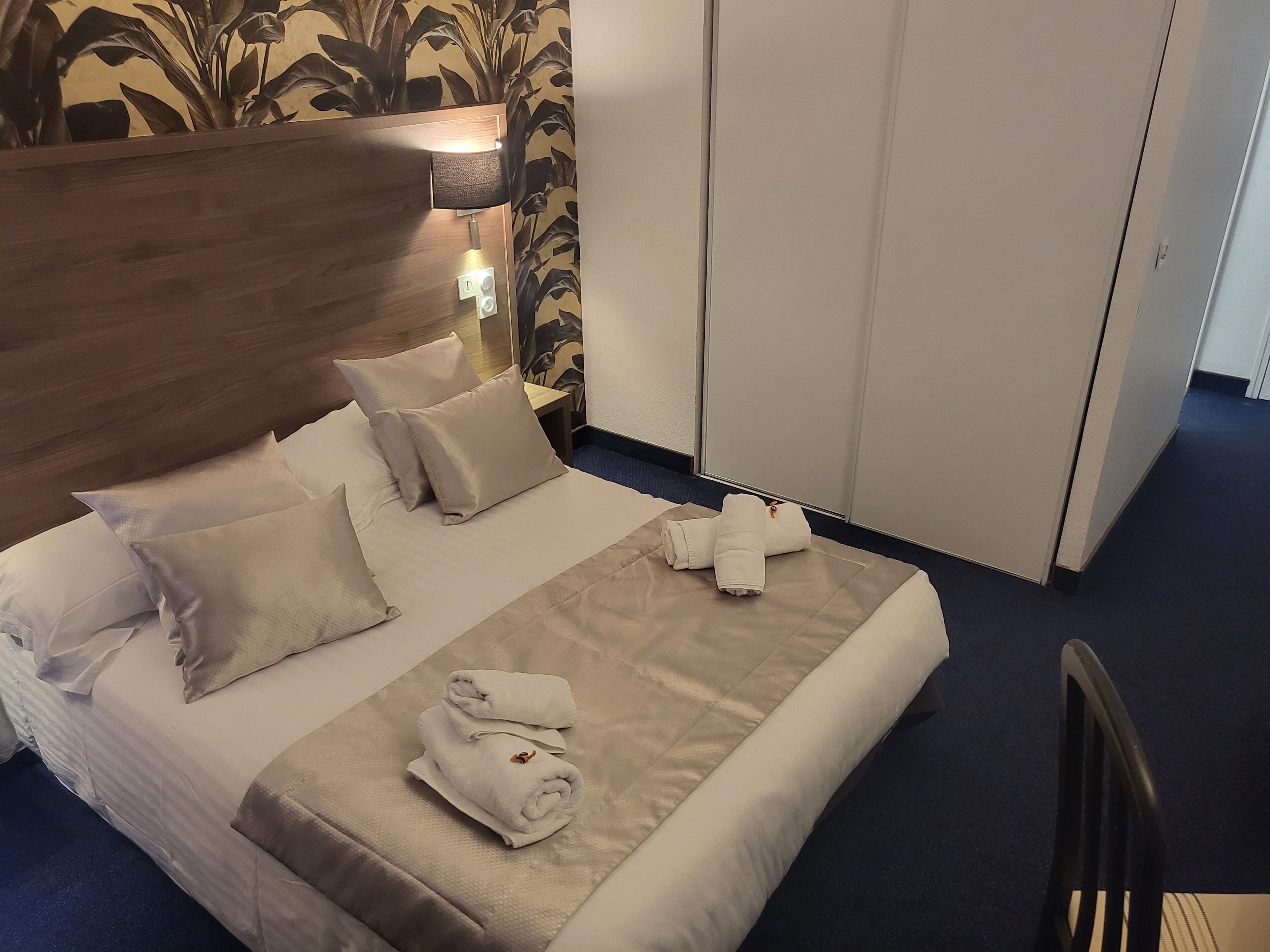 A hotel room with a bed, pillows, a bedside lamp, a wardrobe, and a chair.