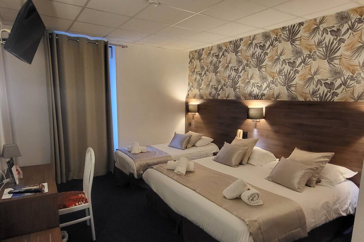 Ein Hotelzimmer mit zwei Betten, einem Schreibtisch, einem Stuhl und einem Fernseher.