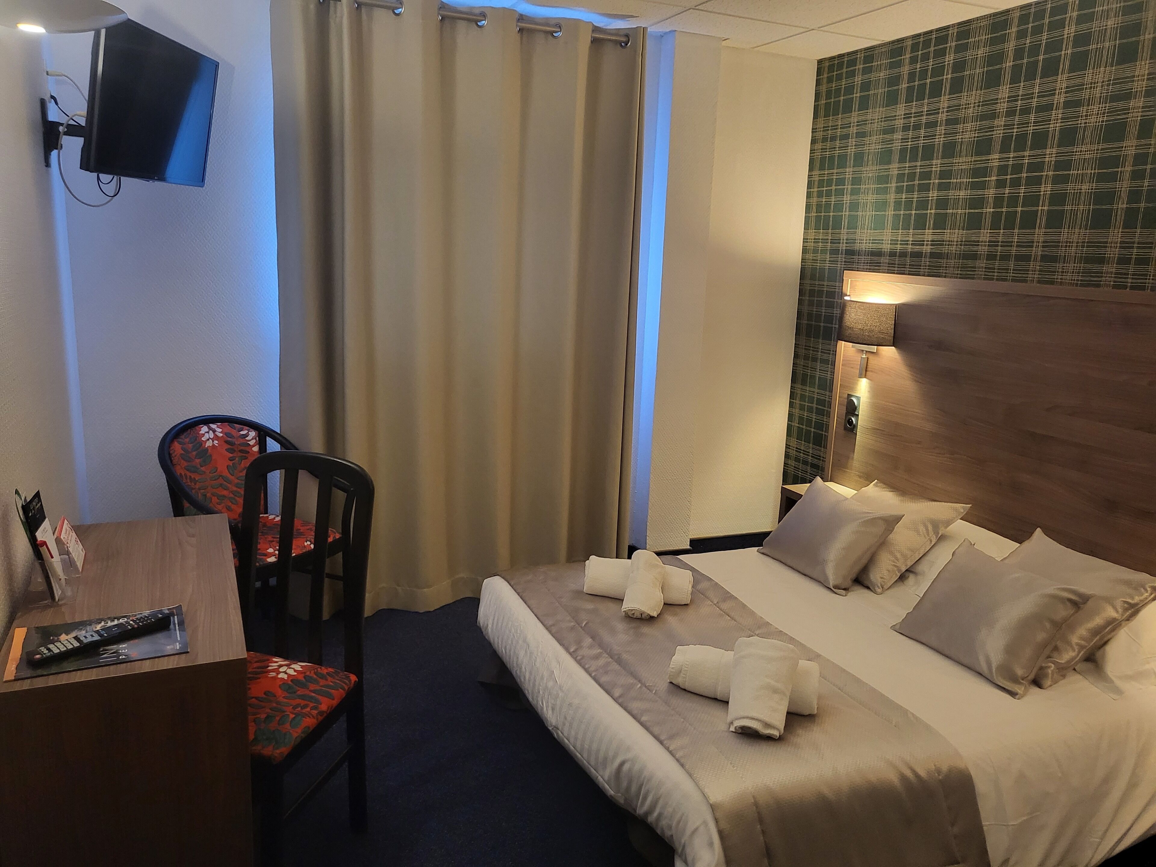 Ett hotellrum med en säng, ett skrivbord med en fjärrkontroll, en stol och en tv som är monterad på väggen.