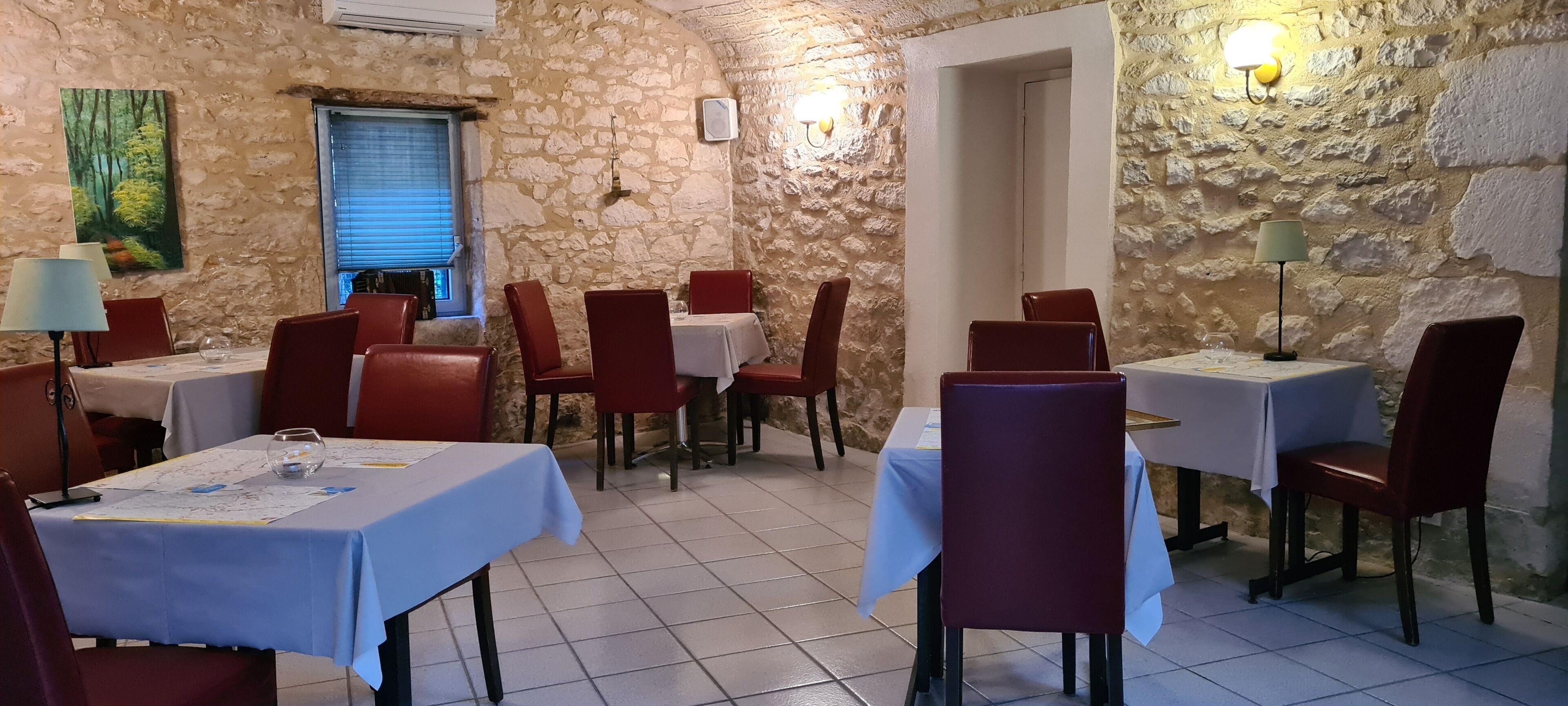A restaurant with stone walls, red chairs, and tables covered with white tablecloths.