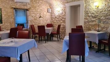 A restaurant with stone walls, red chairs, and tables covered with white tablecloths.