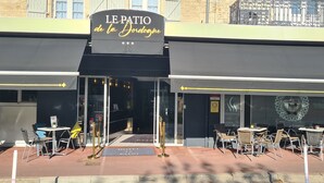 The exterior of Le Patio de la Jordogne, featuring outdoor seating with metal chairs and tables, a black awning, and a sign above the entrance.