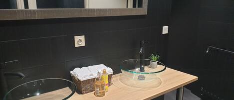 A modern bathroom with two glass sinks, a large mirror, and a small potted plant.