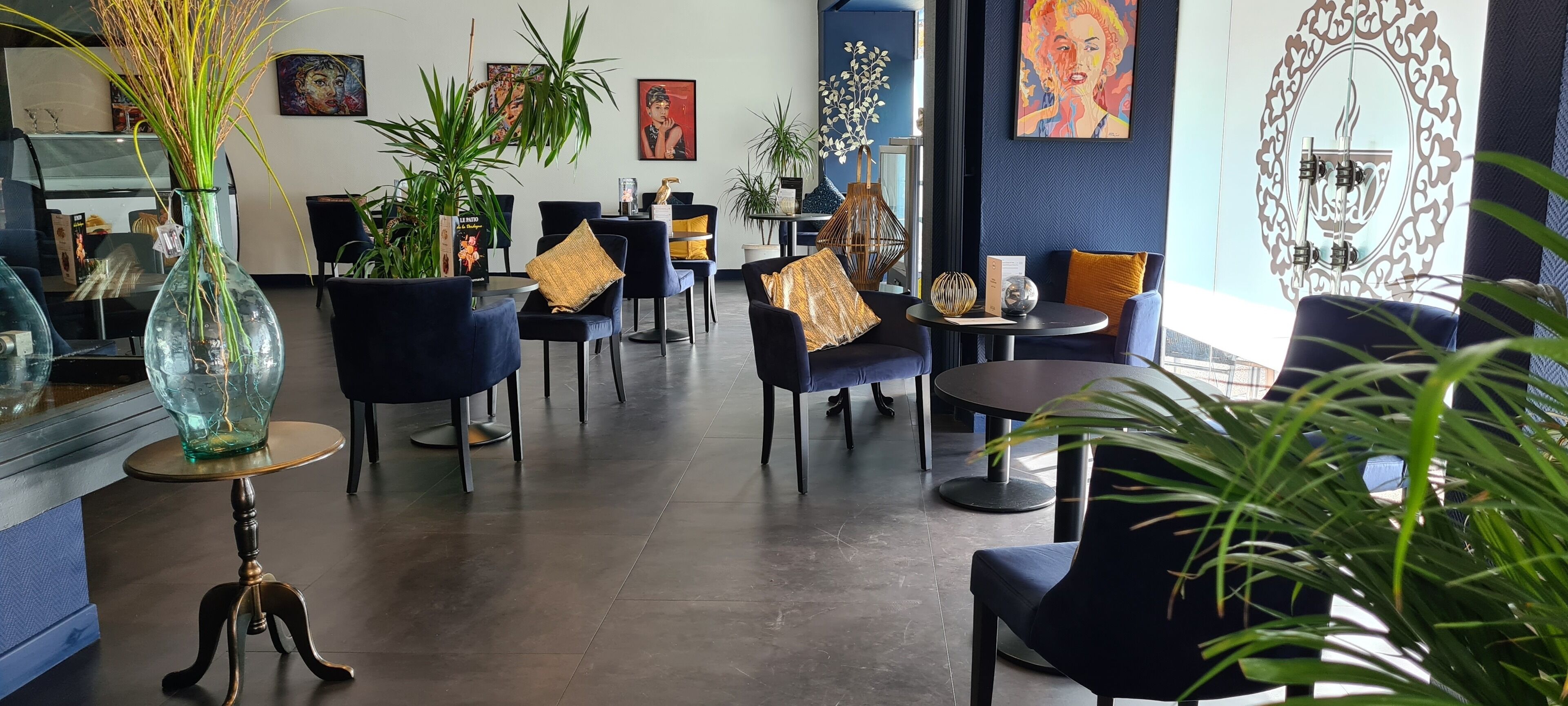 Un interno moderno con sedie blu scuro, tavoli rotondi e piante decorative.