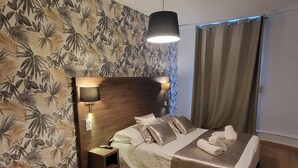 A neatly made bed with pillows and a blanket, a bedside table with a lamp, and a patterned wallpaper.
