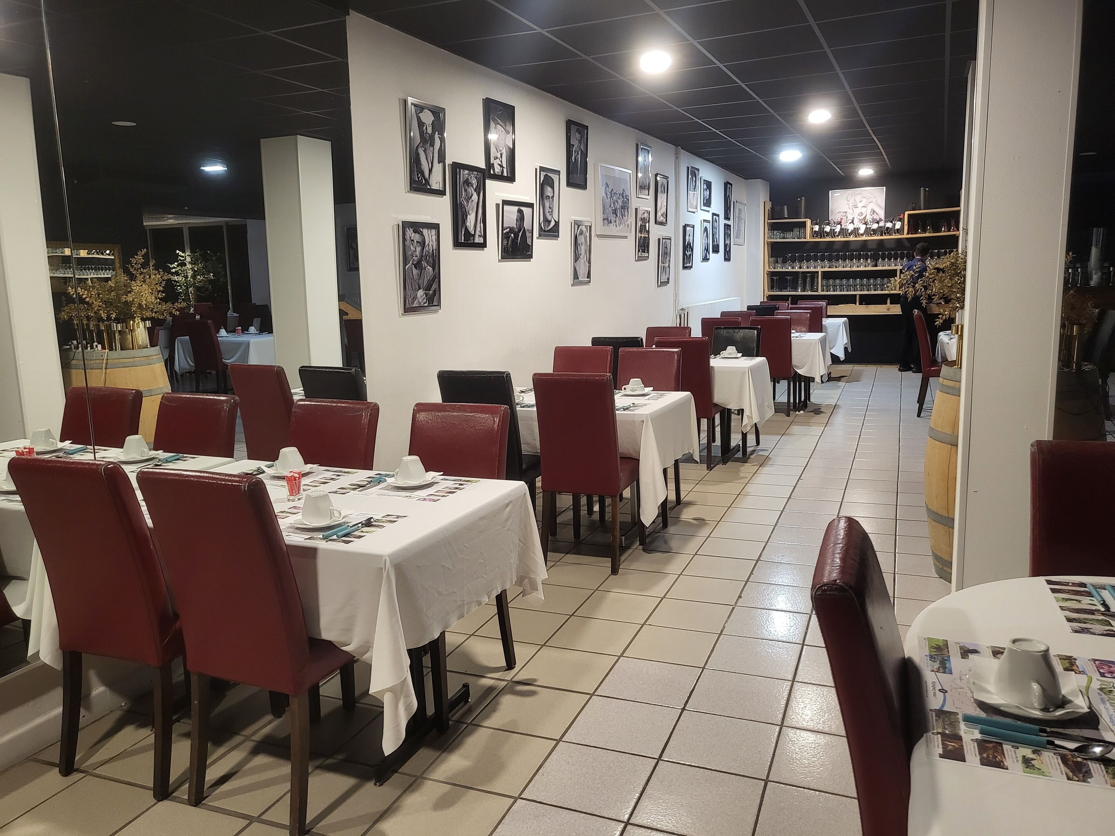 A restaurant with tables set for dining, red chairs, and a wall adorned with framed pictures.