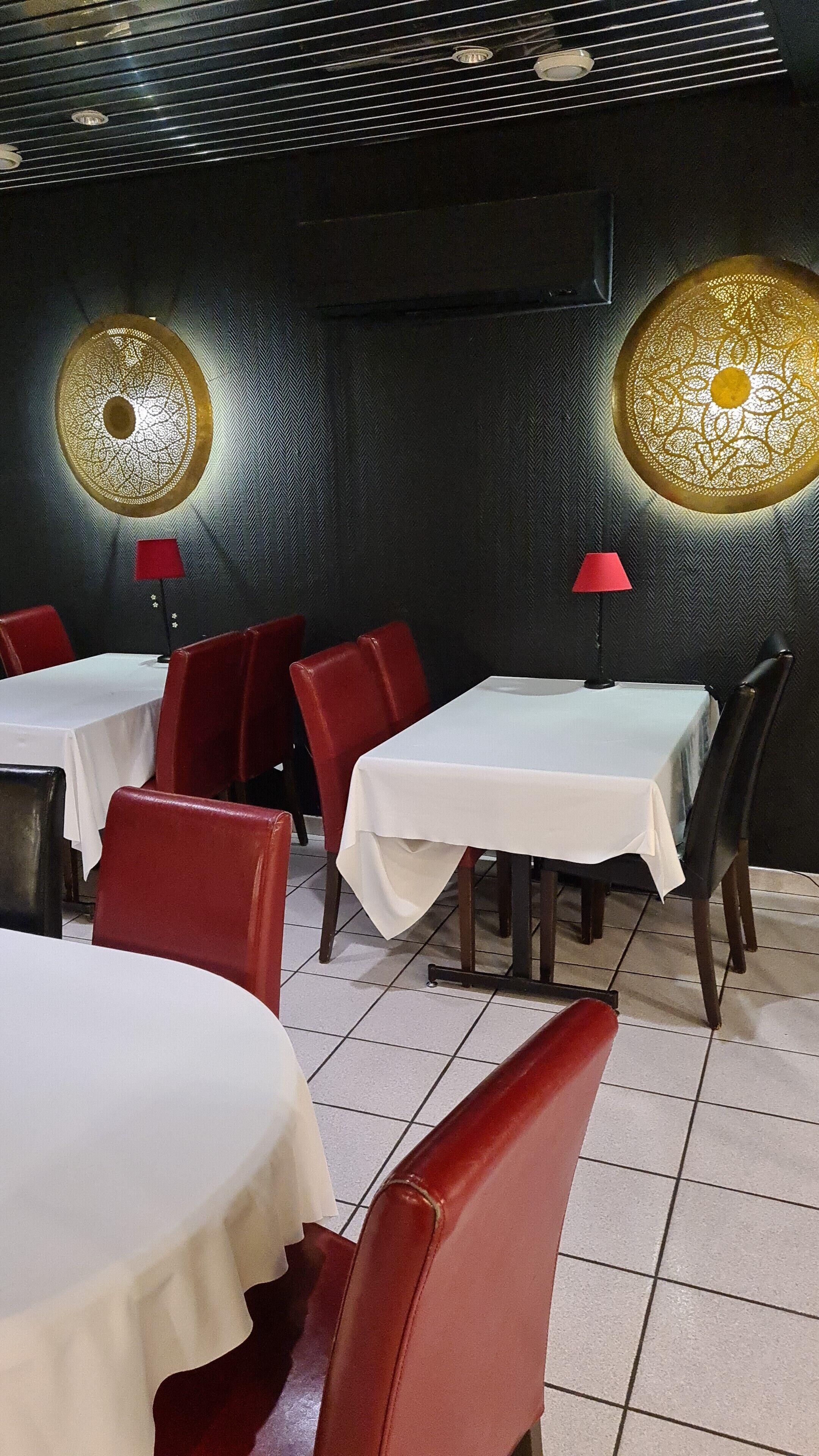 L’intérieur d’un restaurant, avec des tables et des chaises, un plafond à motifs et une chaise rouge au premier plan.