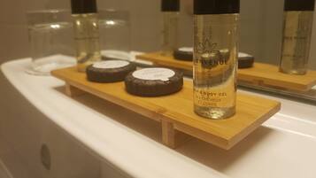 Un meuble-lavabo de salle de bain avec un miroir, un lavabo blanc et une étagère en bois contenant divers articles de toilette, notamment un flacon étiqueté « VENUE » et deux récipients ronds.