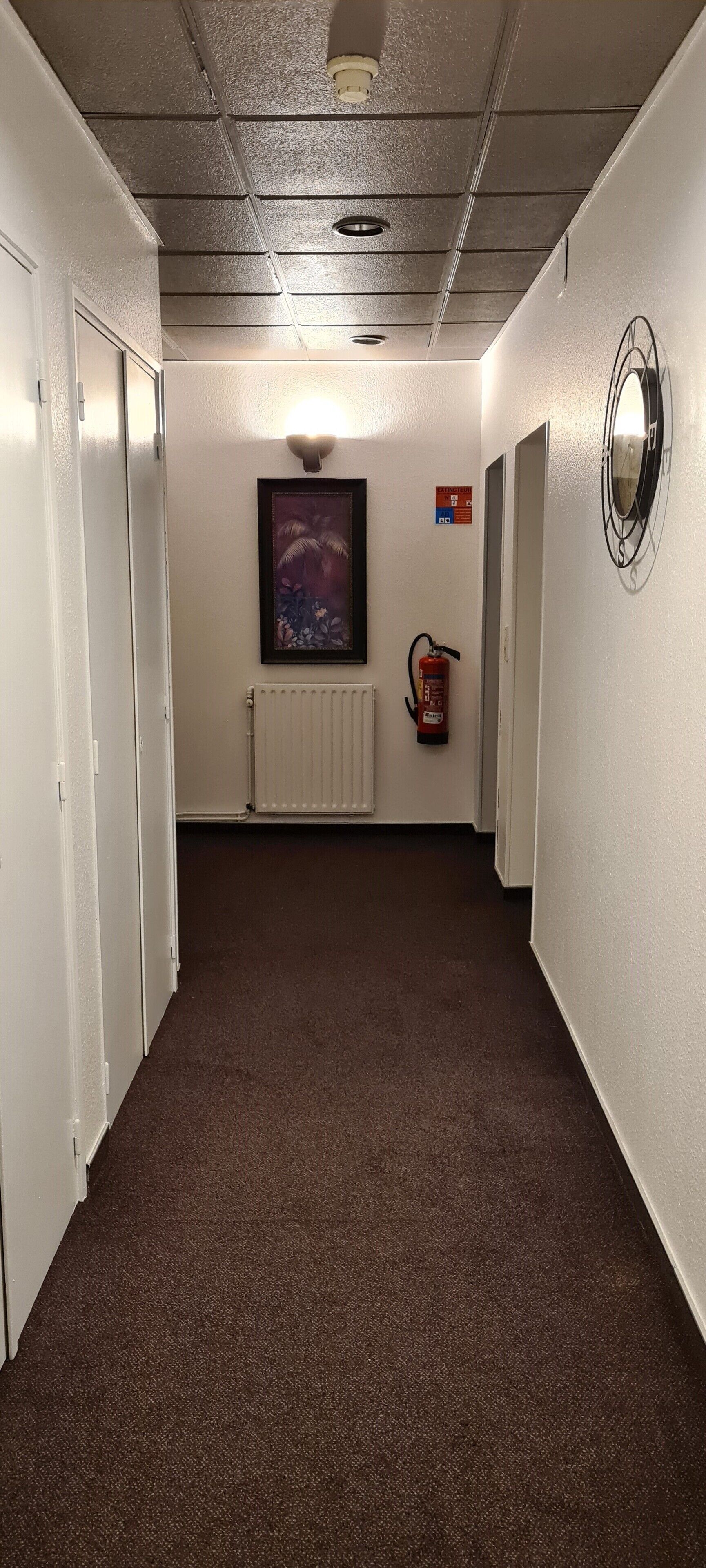 A hallway with carpeted floors, white walls, and a fire extinguisher mounted on the wall.