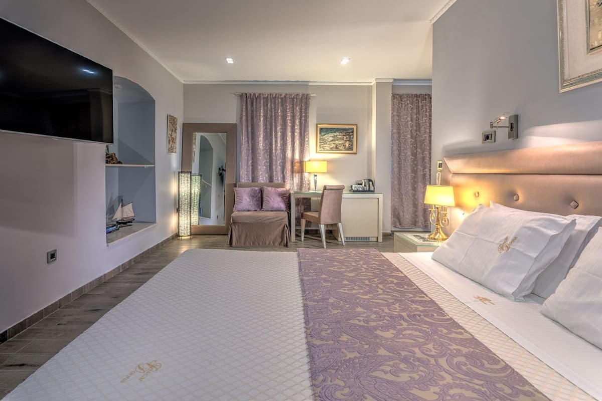 Quarto de hotel com uma cama grande, uma escrivaninha com cadeira, televisão na parede e uma janela com cortinas.