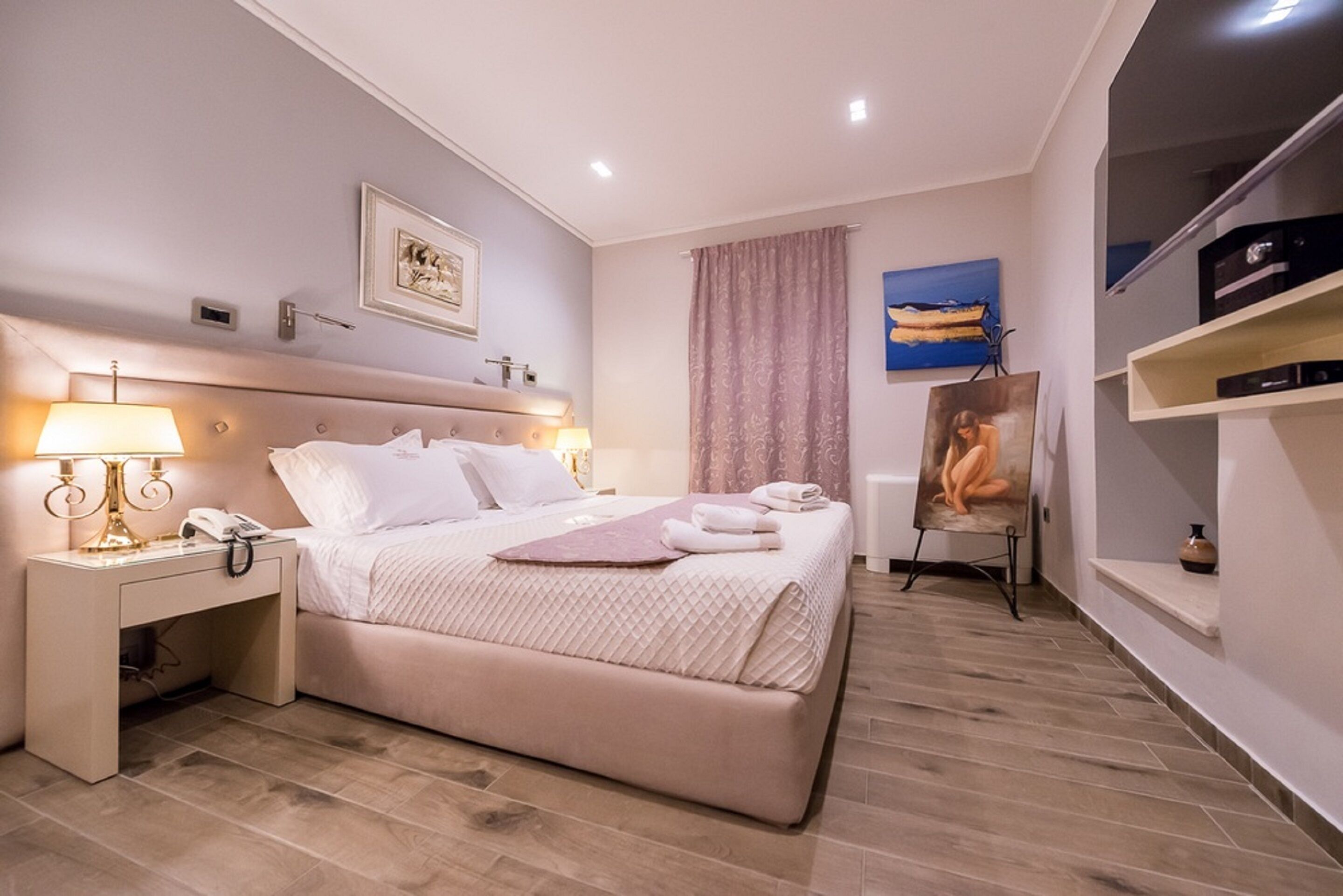 A hotel room with a bed, bedside tables, a lamp, a painting, and a shelf with items.