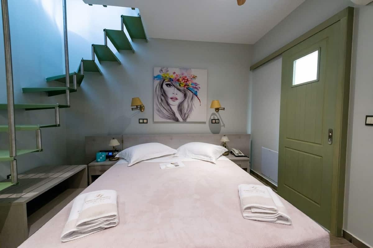 Quarto de hotel com cama, duas luminárias de cabeceira, mesa de cabeceira, porta verde e um quadro na parede.