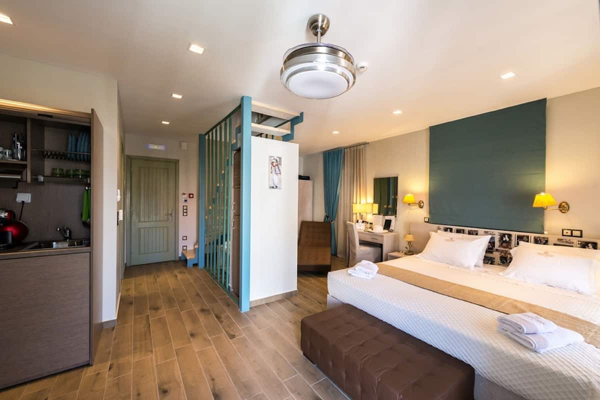 Quarto de hotel com uma cama, secretária, cadeira, guarda-roupa e cozinha compacta.