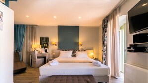 Ein Hotelzimmer mit einem großen Bett, einem Schreibtisch, einem Sessel, einem Fernseher und einem Vorhangfenster.