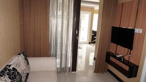 Habitación de hotel con cama, televisor sobre un soporte de madera y vista al pasillo.