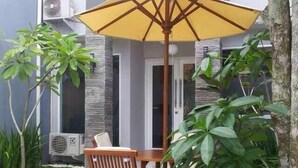 Una casa de huéspedes familiar con un letrero, una silla de madera, una mesa y un paraguas amarillo.