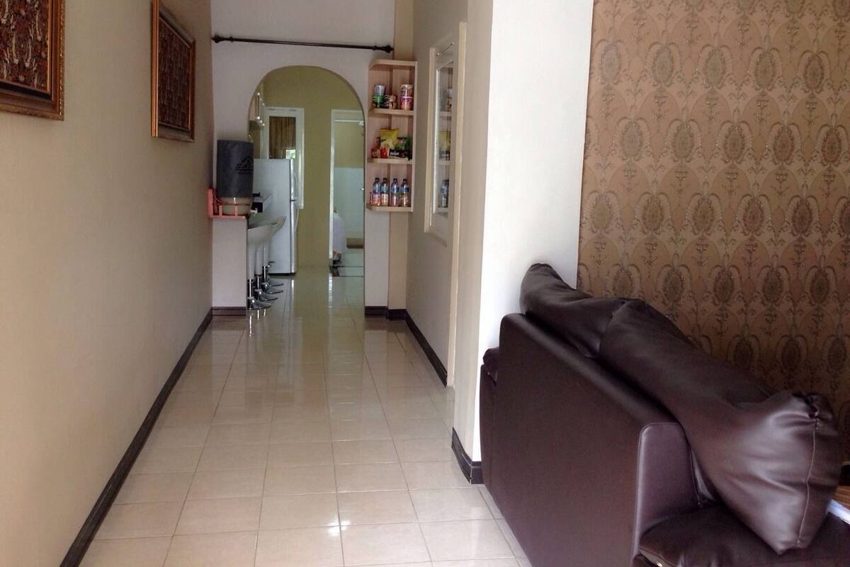 A hallway with a brown leather sofa, a kitchen area, and a patterned wallpaper wall.