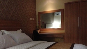 Habitación de hotel con una cama grande, un armario de madera, un escritorio con espejo y una alfombra estampada.