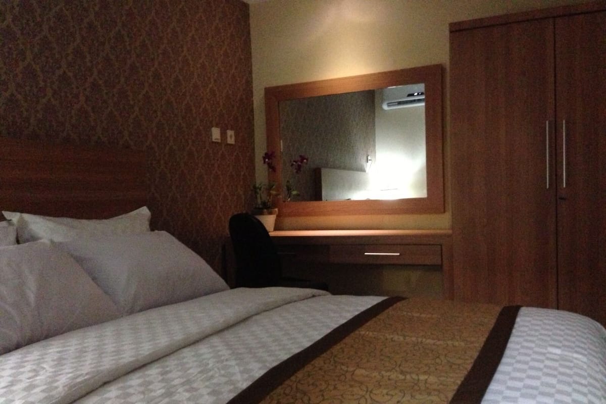 A hotel room with a large bed, a wooden wardrobe, a desk with a mirror, and a patterned carpet.