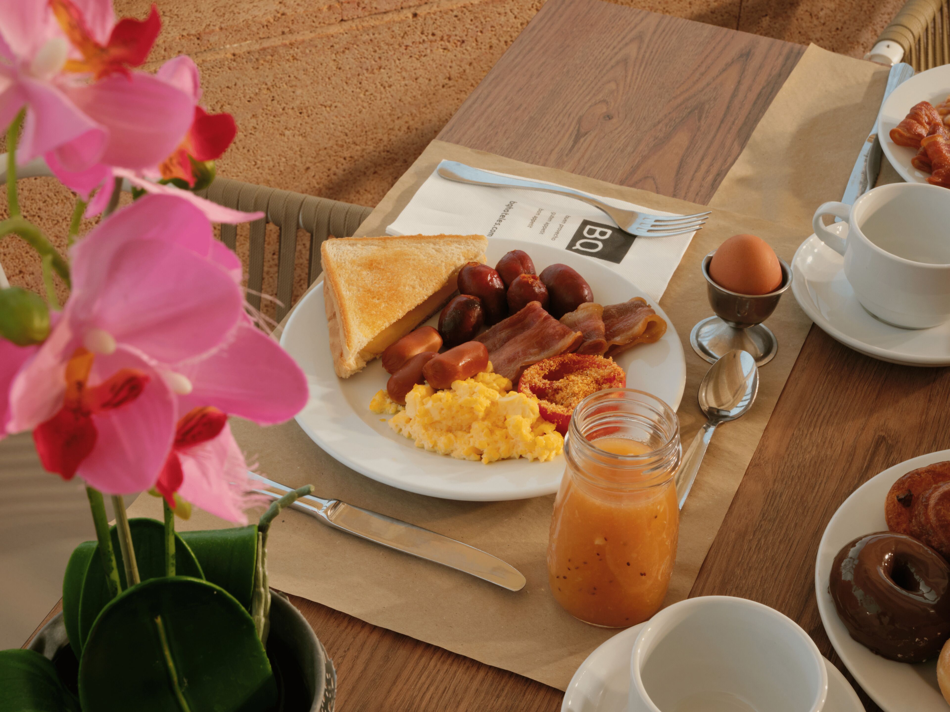 Une assiette de petit-déjeuner comprenant des toasts, des saucisses, du bacon, des œufs brouillés et un verre de jus d’orange.