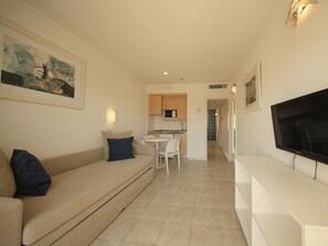 A living room with a sofa, a TV, and a kitchen in the background. - BQ Alcudia Sun Village - All Inclusive (Muro)