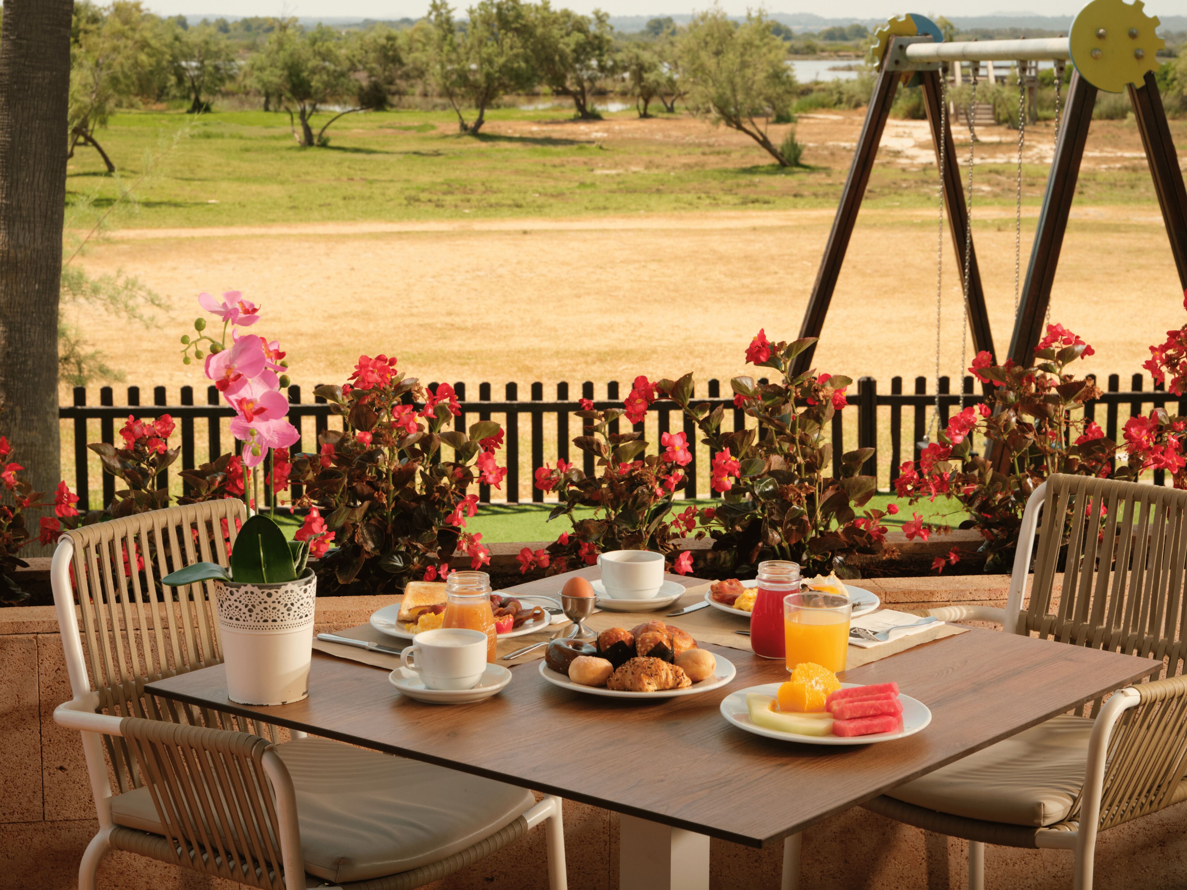 A breakfast table set outdoors with a view of a fenced field and trees.