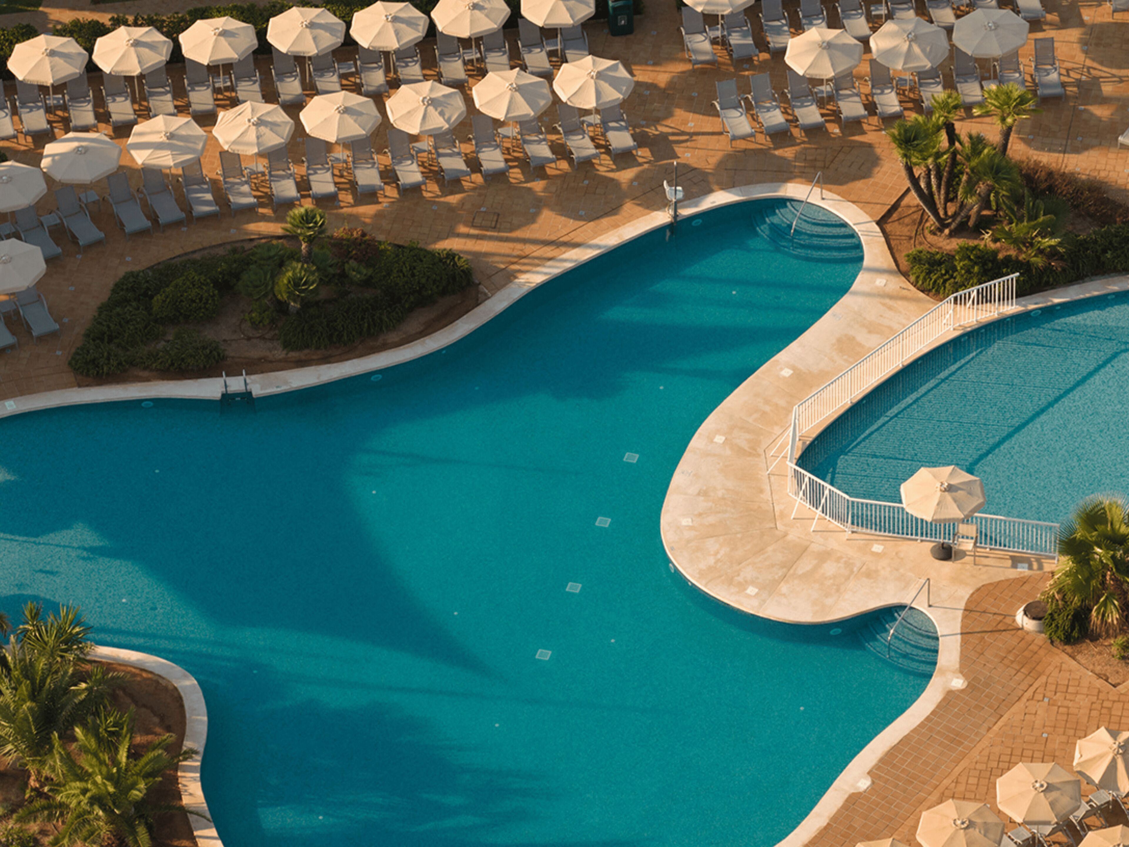 A large swimming pool with a curved edge, surrounded by lounge chairs and umbrellas.